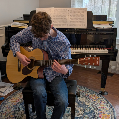 Emmett Axelrod playing guitar in front of a piano